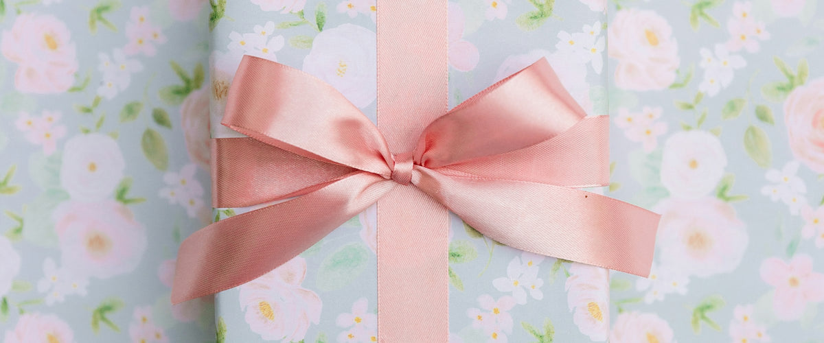 A gift wrapped with a pink ribbon on a floral background
